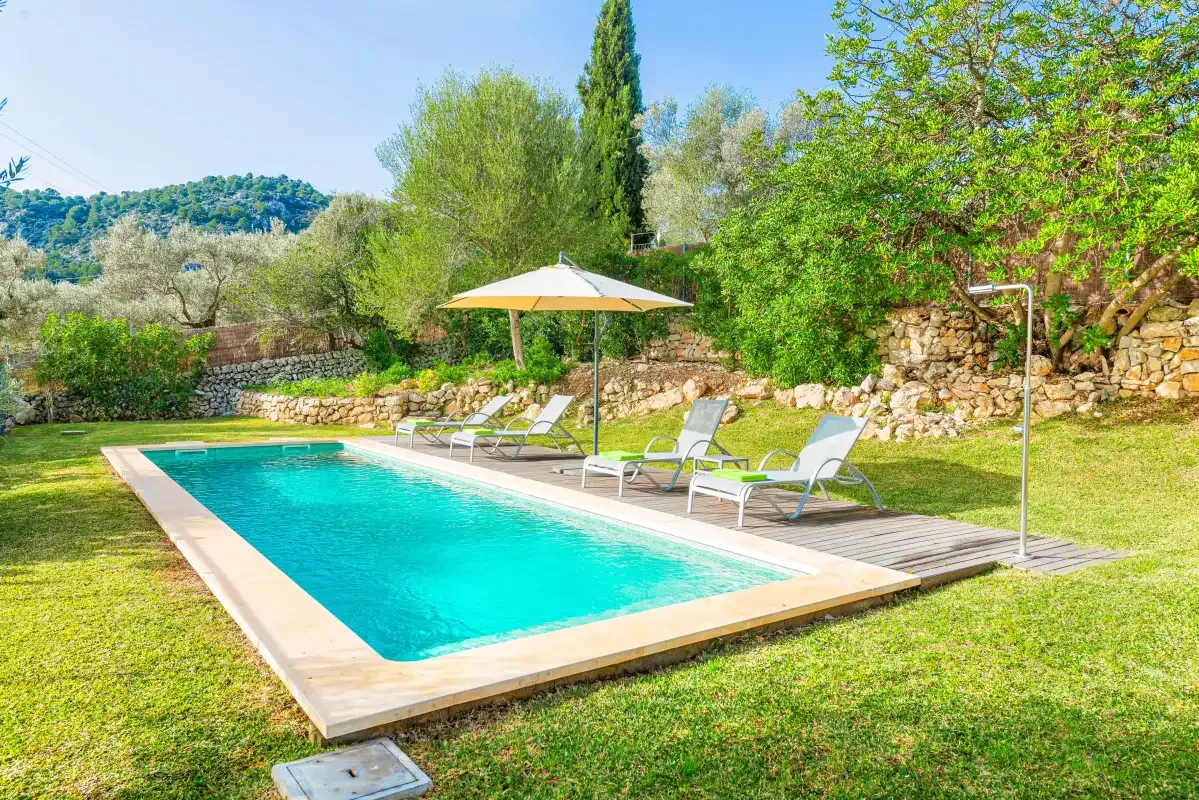 An outdoor swimming pool bordered by grass, with loungers and an umbrella nearby.