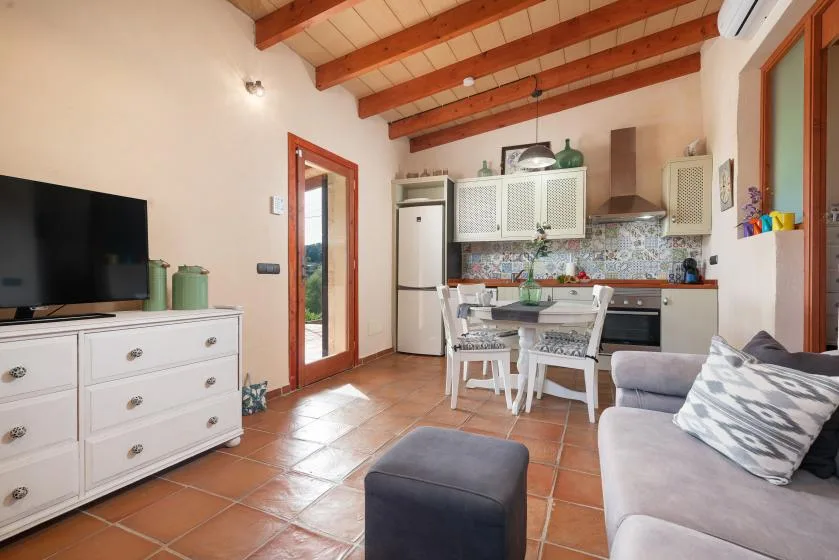 A combined living room and kitchen with a dining table and exposed ceiling beams.