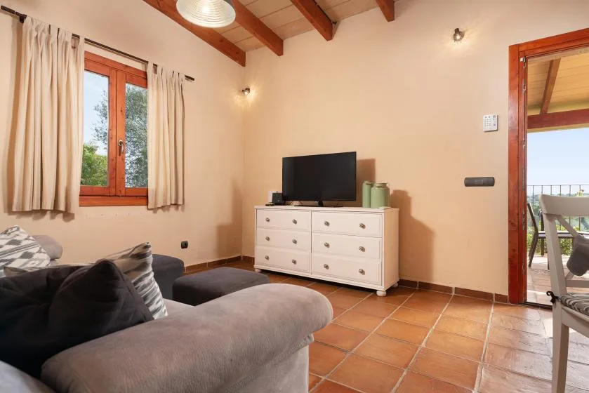 A living room with seating, a television, and a window overlooking greenery.