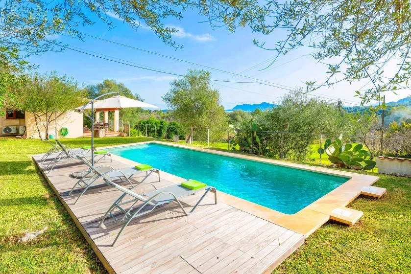 An outdoor swimming pool sits beside a wooden deck with loungers and greenery.