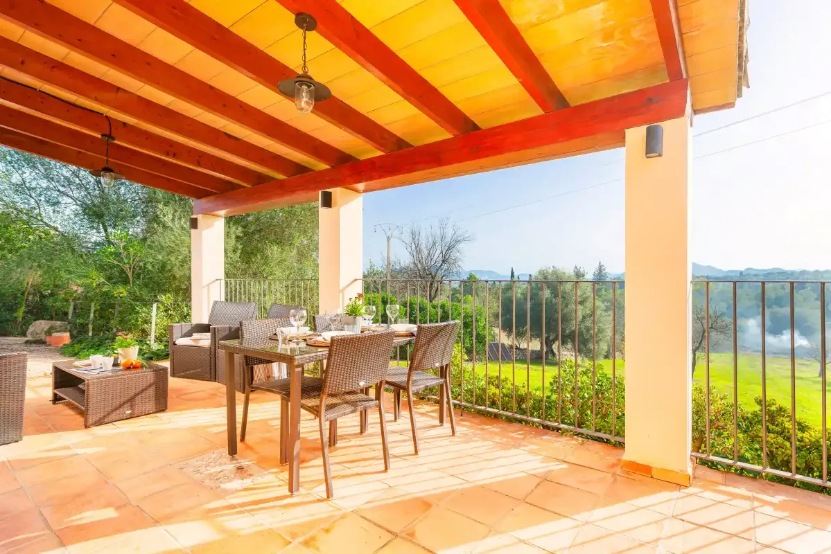 A covered patio has a dining table and seating overlooking a garden.