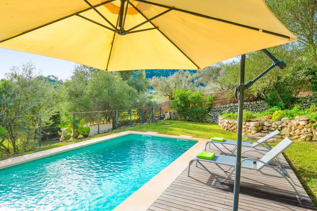 An outdoor swimming pool beside a wooden deck with lounge seating and a large umbrella.