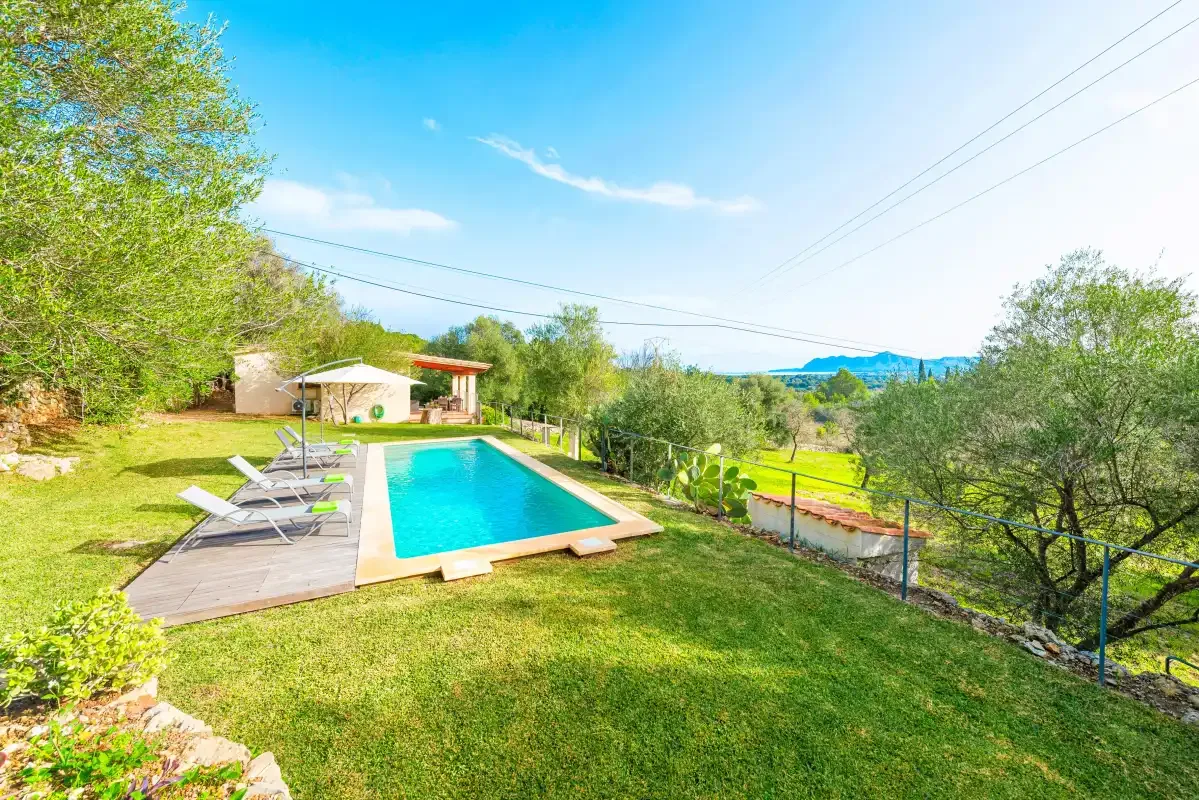 An outdoor swimming pool beside a grassy yard and rows of lounge seating.