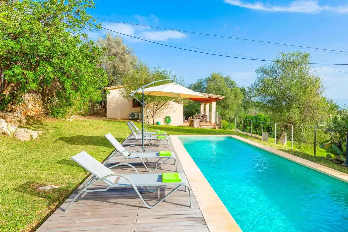 An outdoor swimming pool beside a deck with loungers and a shaded seating area.