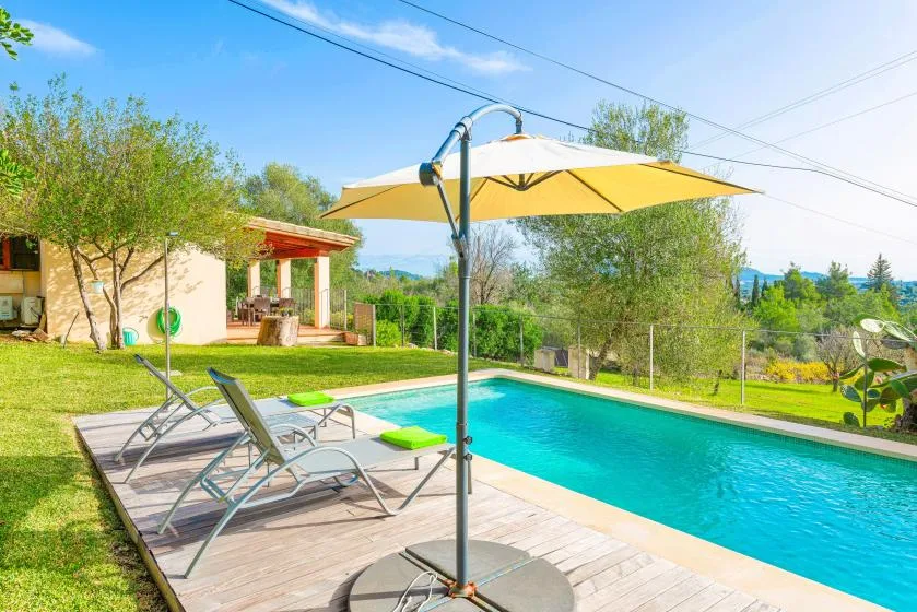 An outdoor swimming pool beside a wooden deck with reclining seats and a yellow umbrella.