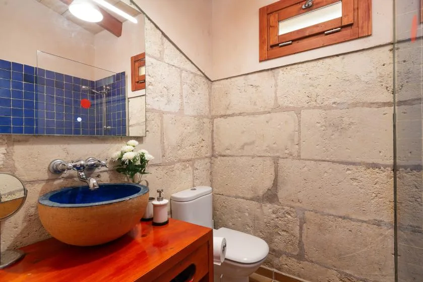 A bathroom with a blue vessel sink, toilet, and stone walls.