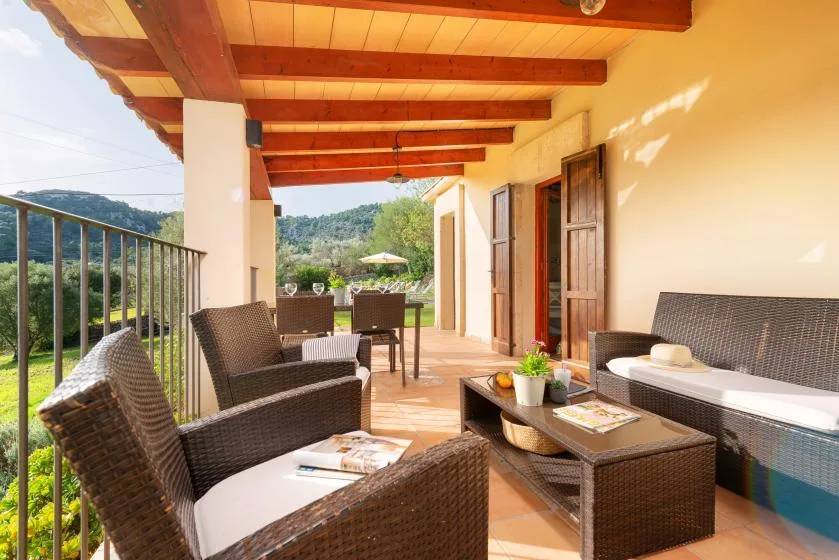 A covered outdoor terrace with wicker seating overlooks a green hillside.