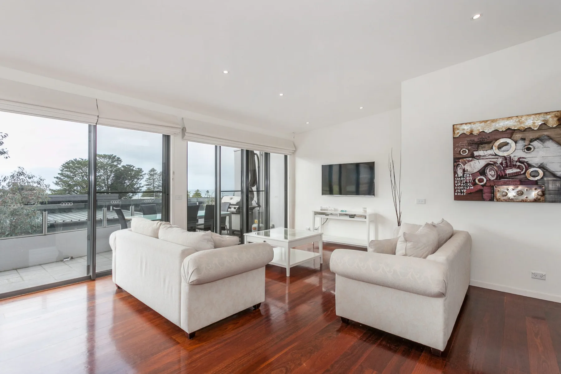 A bright living room with seating, a coffee table, and large windows opening onto a balcony.