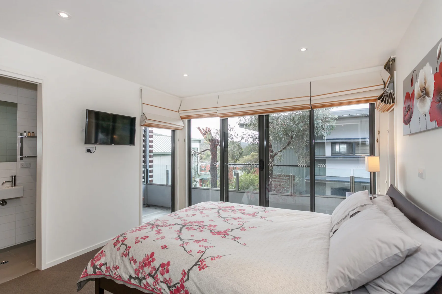 Un dormitorio con una cama frente a grandes ventanas y un balcón.