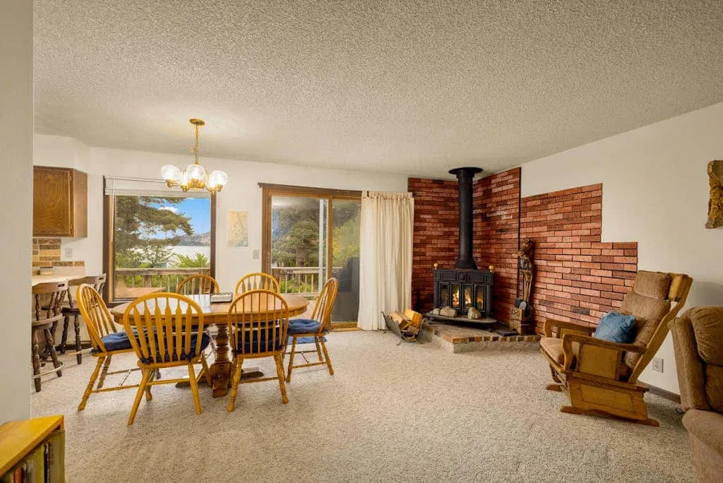 A dining and living area features a wooden table and a brick fireplace.