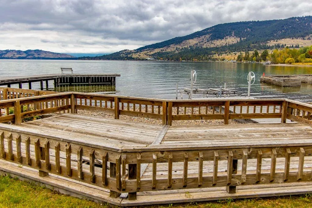 A wooden lakeside deck overlooks the water and wooded hills.