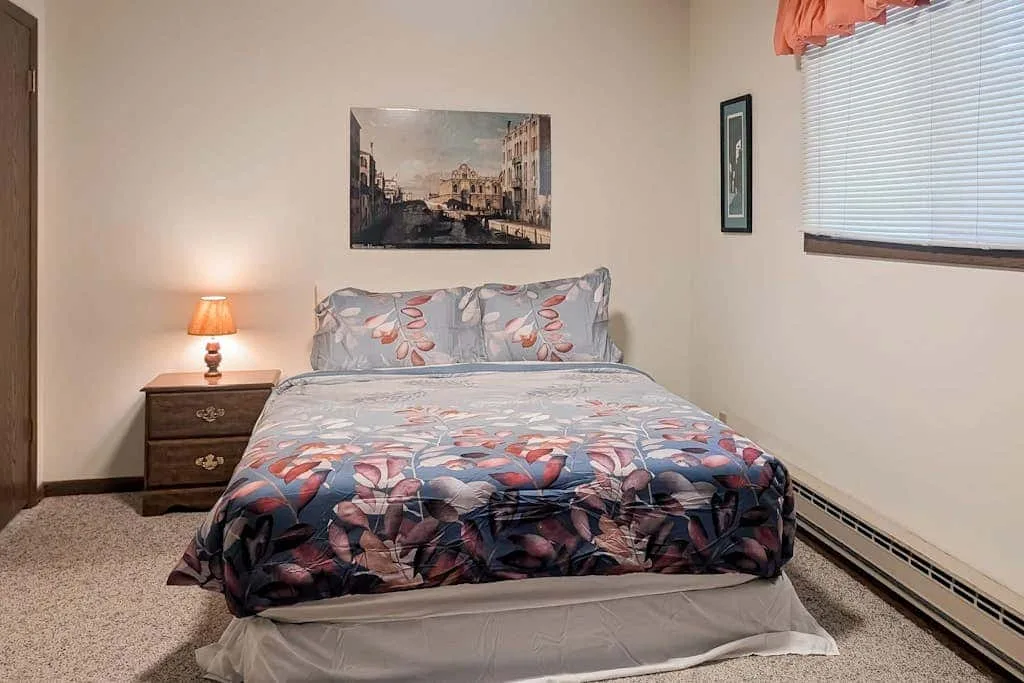 A bedroom with a bed dressed in floral-patterned bedding and a bedside table.