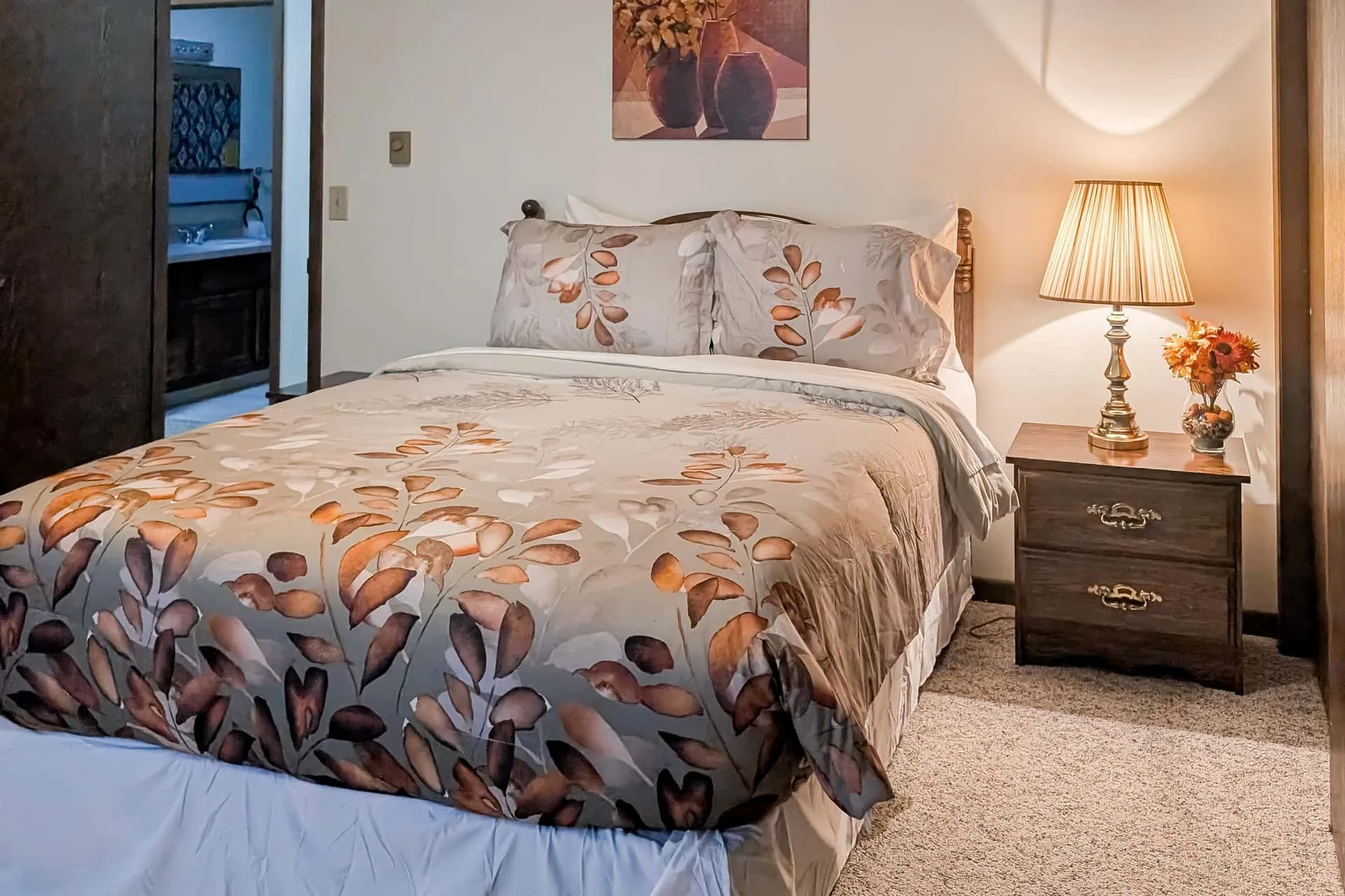 A bedroom with floral bedding and a lit bedside lamp.