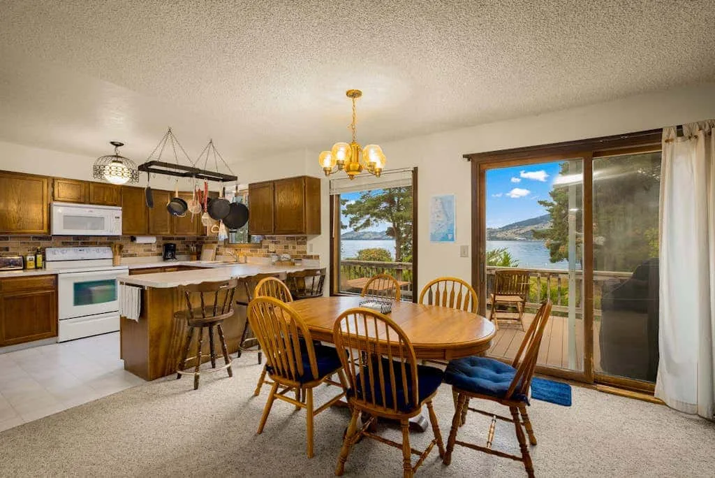 A dining area with a wooden table beside a kitchen and large windows.