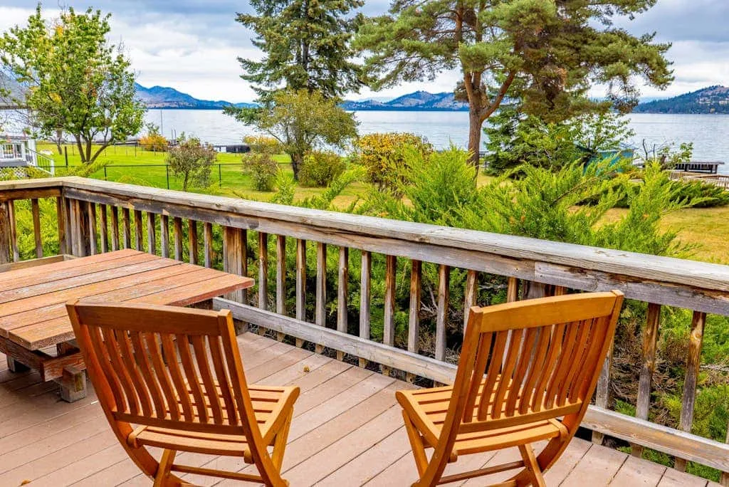 A wooden deck with seating overlooks a landscaped shoreline and the water beyond.