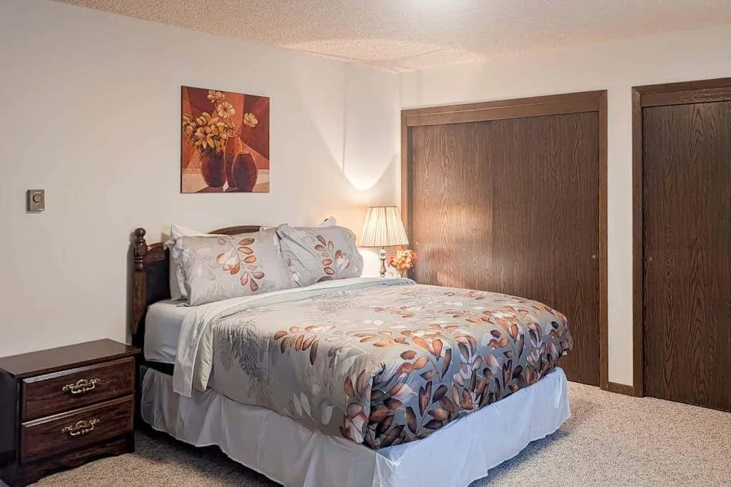 A bedroom with a bed dressed in floral-patterned bedding and a bedside table.