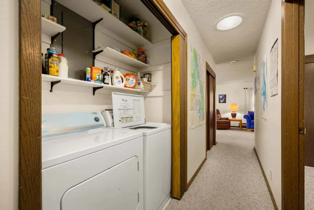 A laundry area with a washer and dryer opens onto a carpeted hallway.