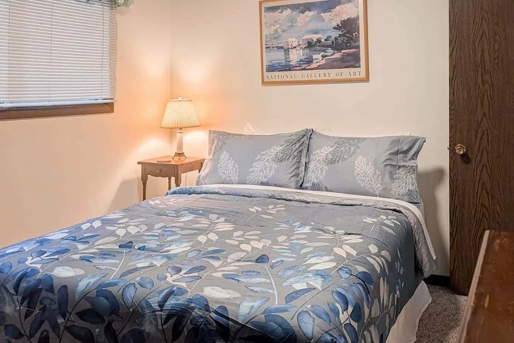 A bedroom with a bed covered in blue floral bedding and a bedside lamp.