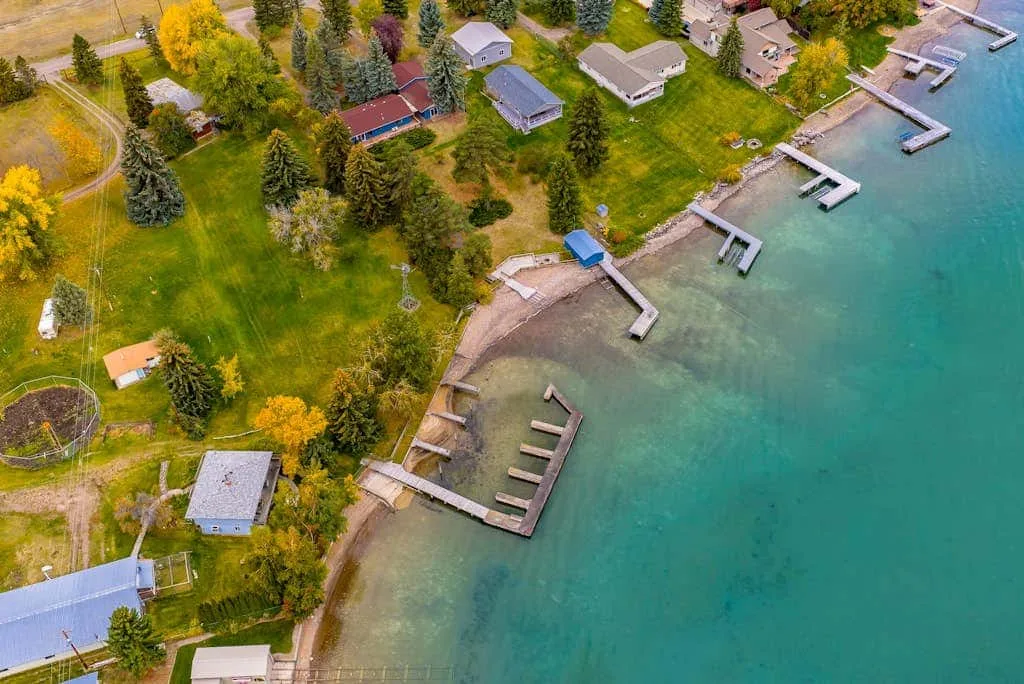 Aerial view of a lakeside shoreline with docks, homes, and green lawns.