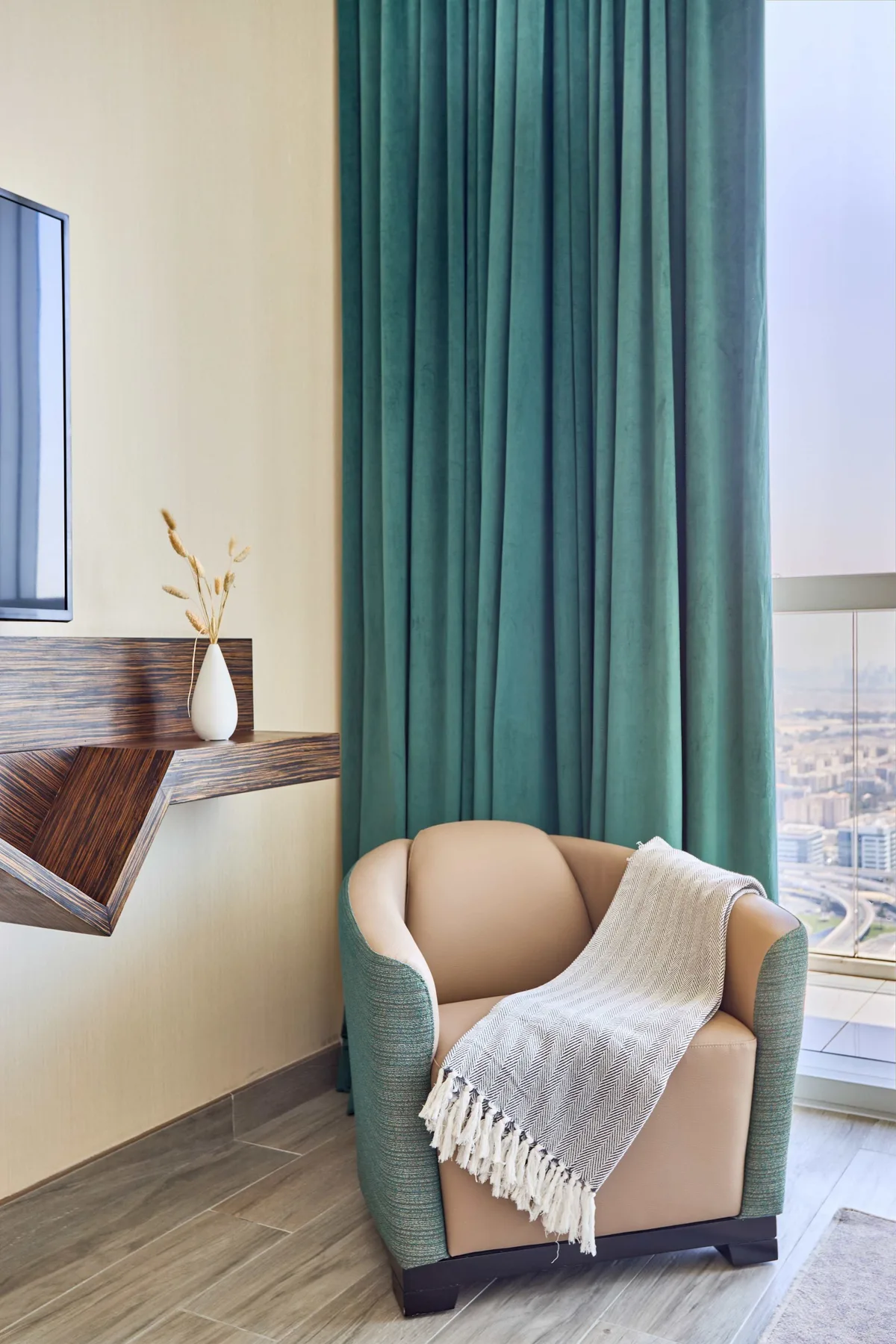 A seating area with a teal armchair beside floor-to-ceiling curtains.