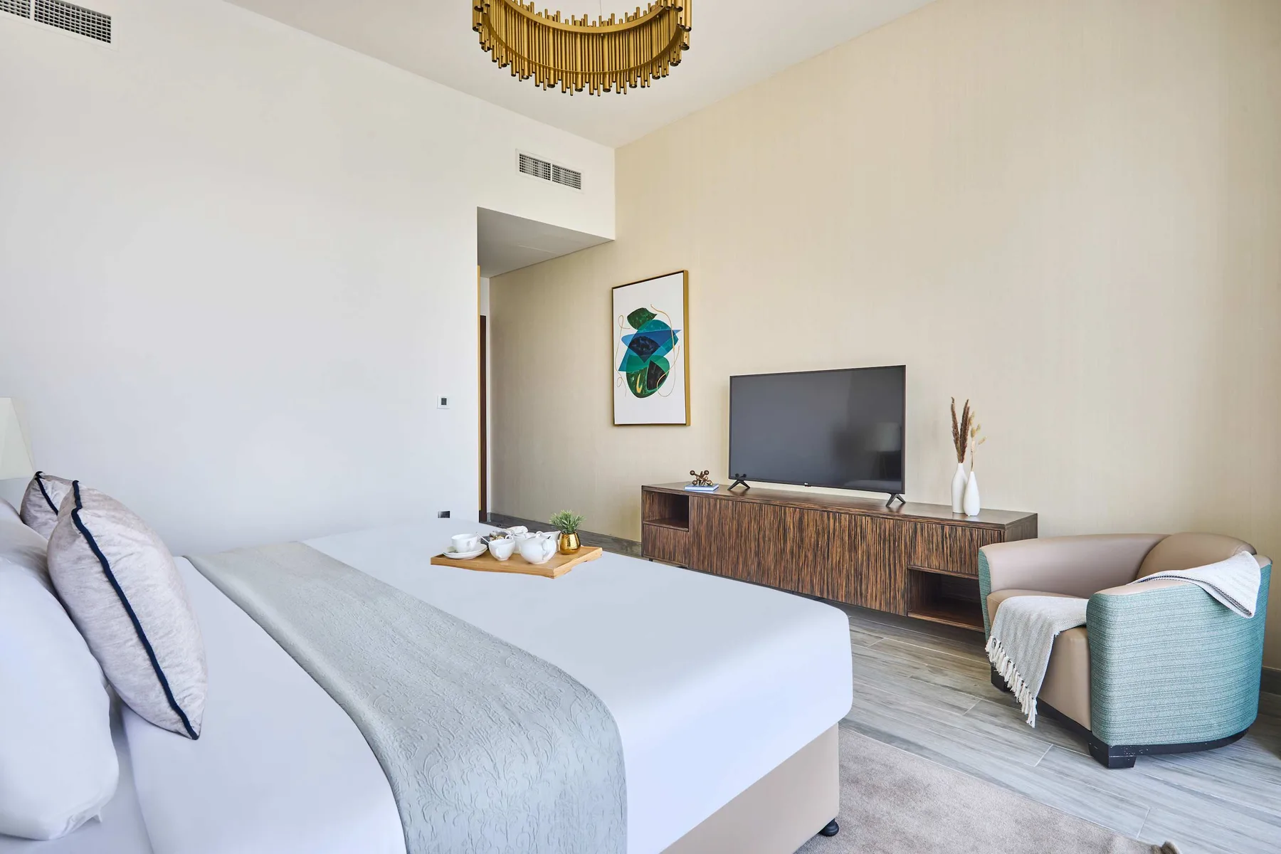 A bright bedroom features a neatly made bed and a television on a wooden console.
