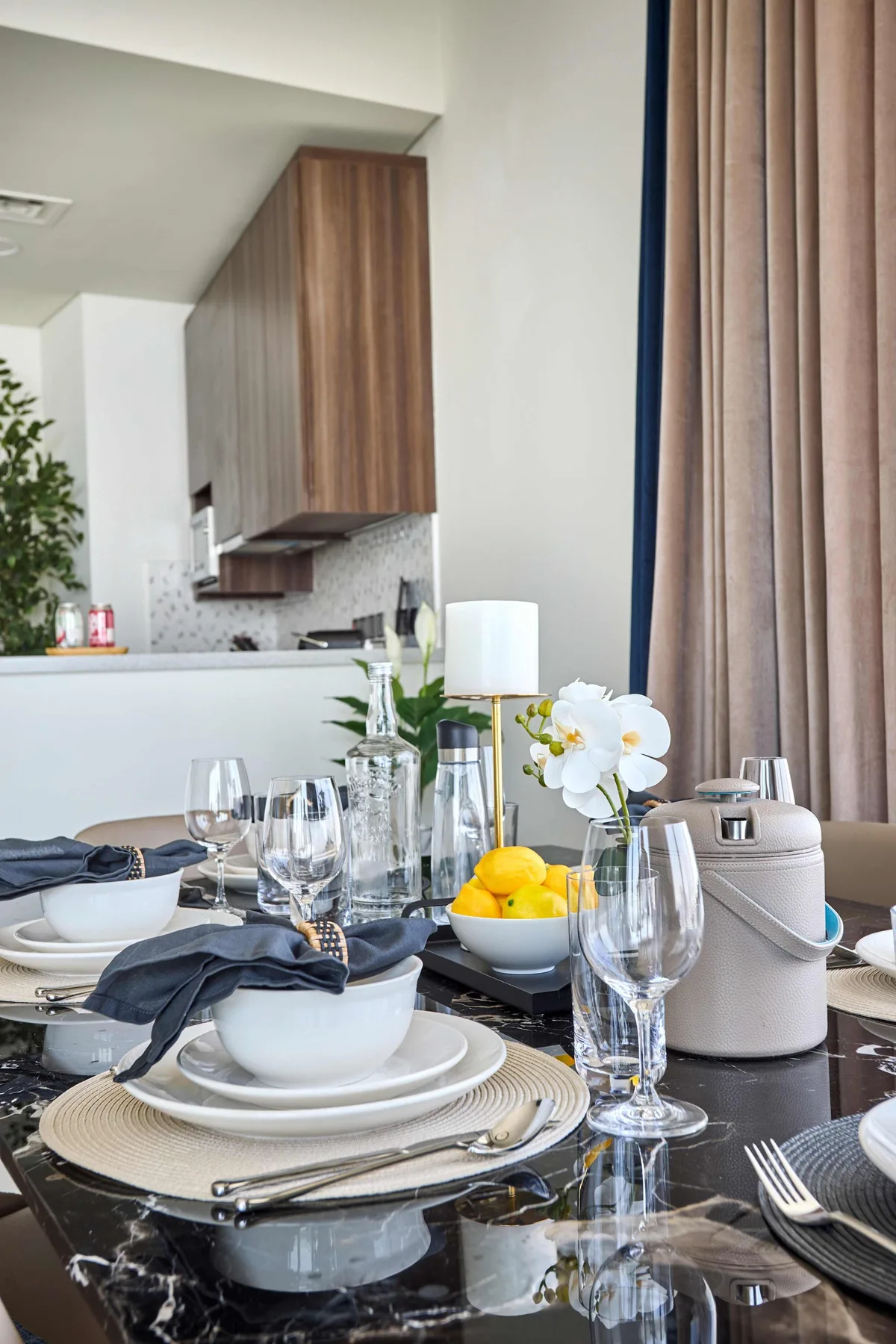 A dining table is set with plates, glassware, fruit, and flowers.