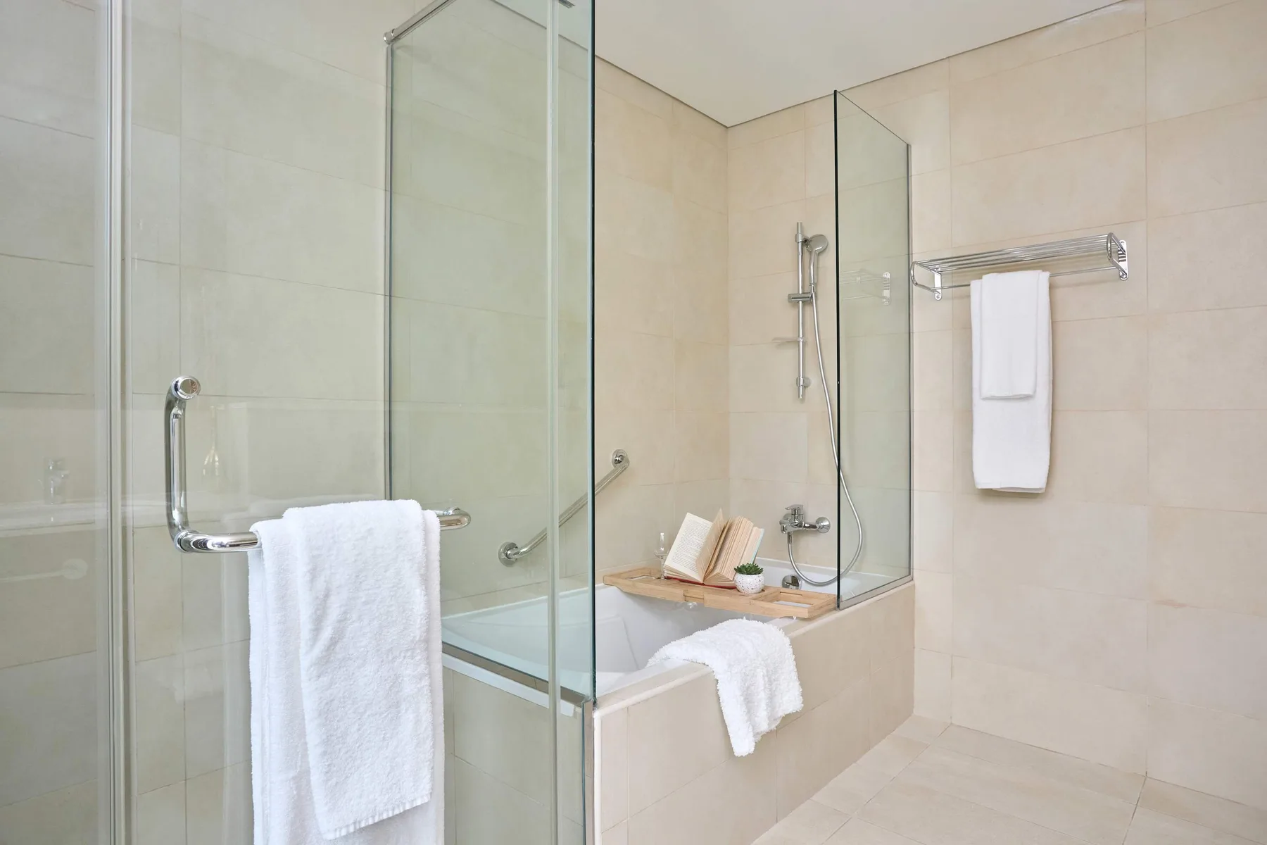 A tiled bathroom with a glass shower enclosure, bathtub, and white towels.