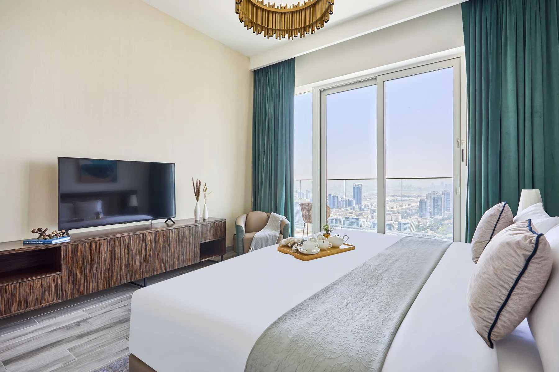 A bright bedroom with a large bed, television, and city views through the window.