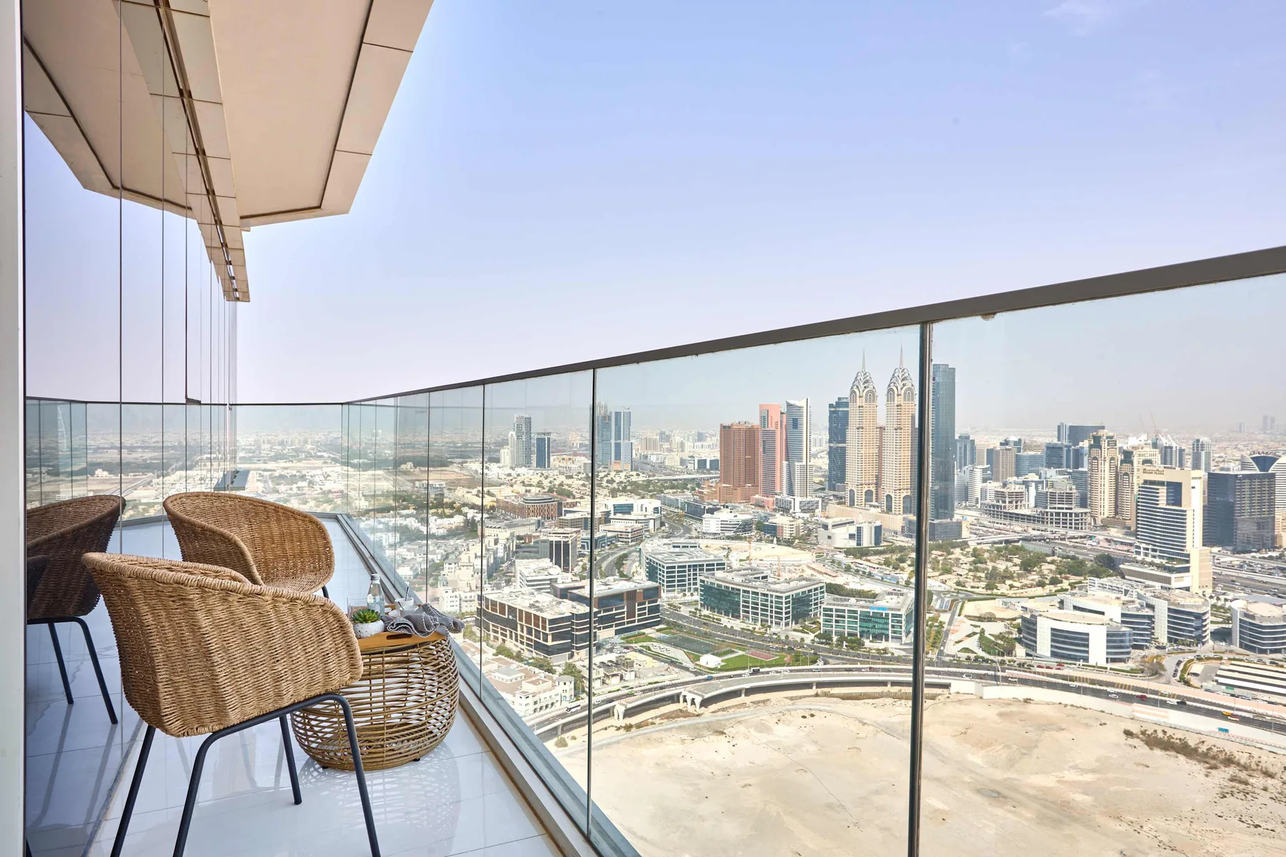 A balcony with woven seating overlooks a city skyline.