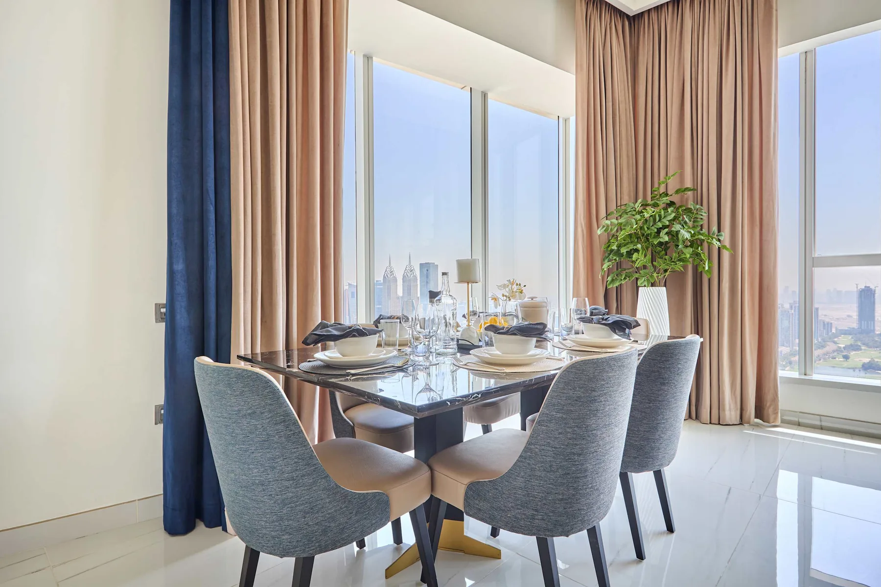 A dining area with a set table beside tall windows and curtains.