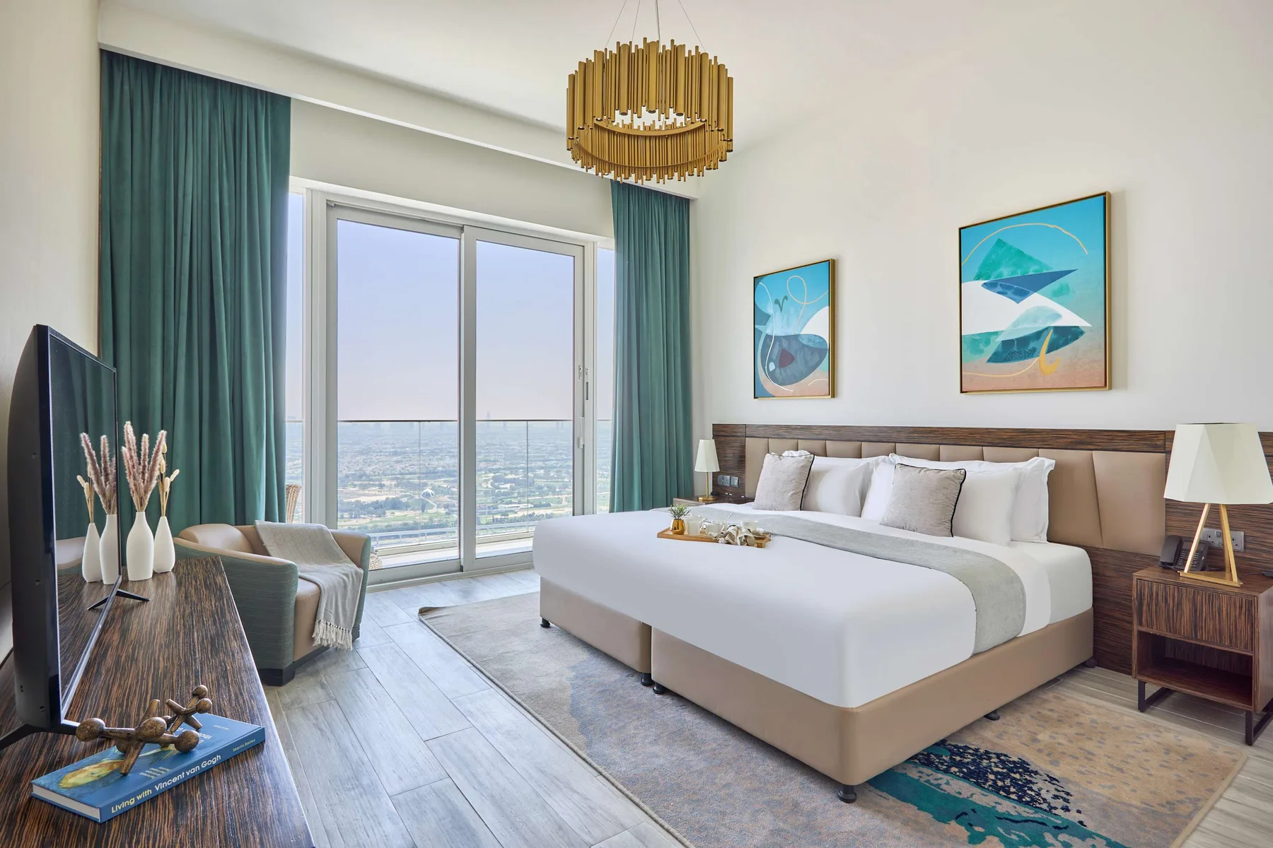 A bright bedroom with a large bed, teal curtains, and framed artwork.
