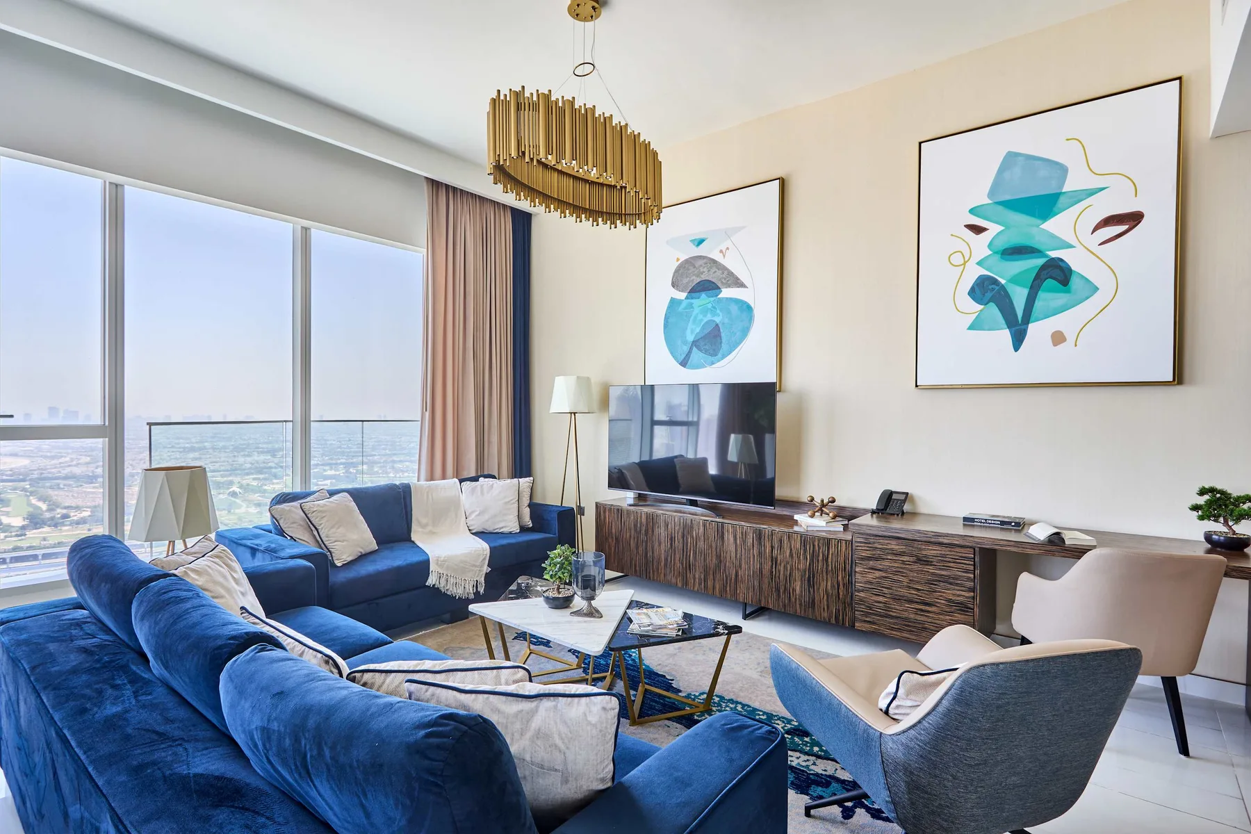A bright living room with blue seating, a television, and large windows overlooking the city.