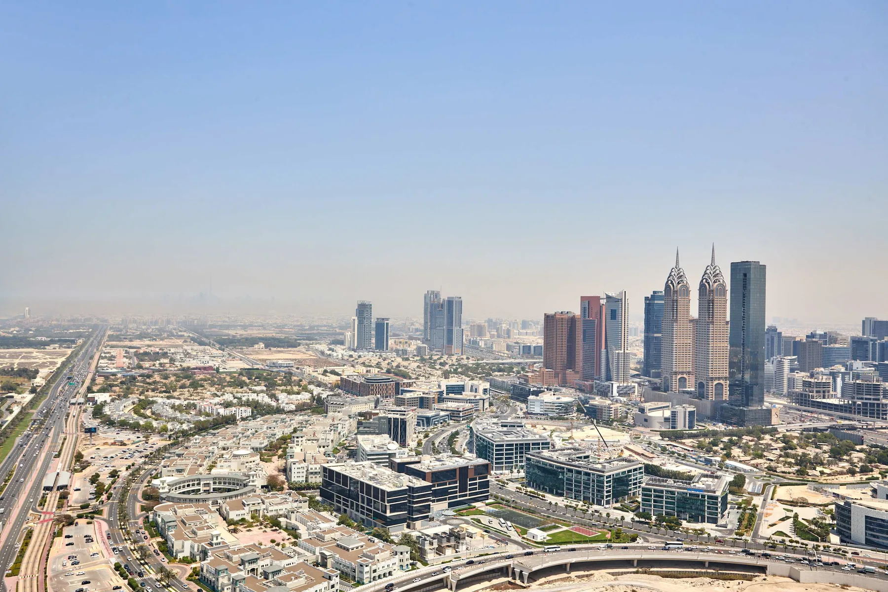 A broad city skyline rises above roads and low-rise buildings under a clear sky.