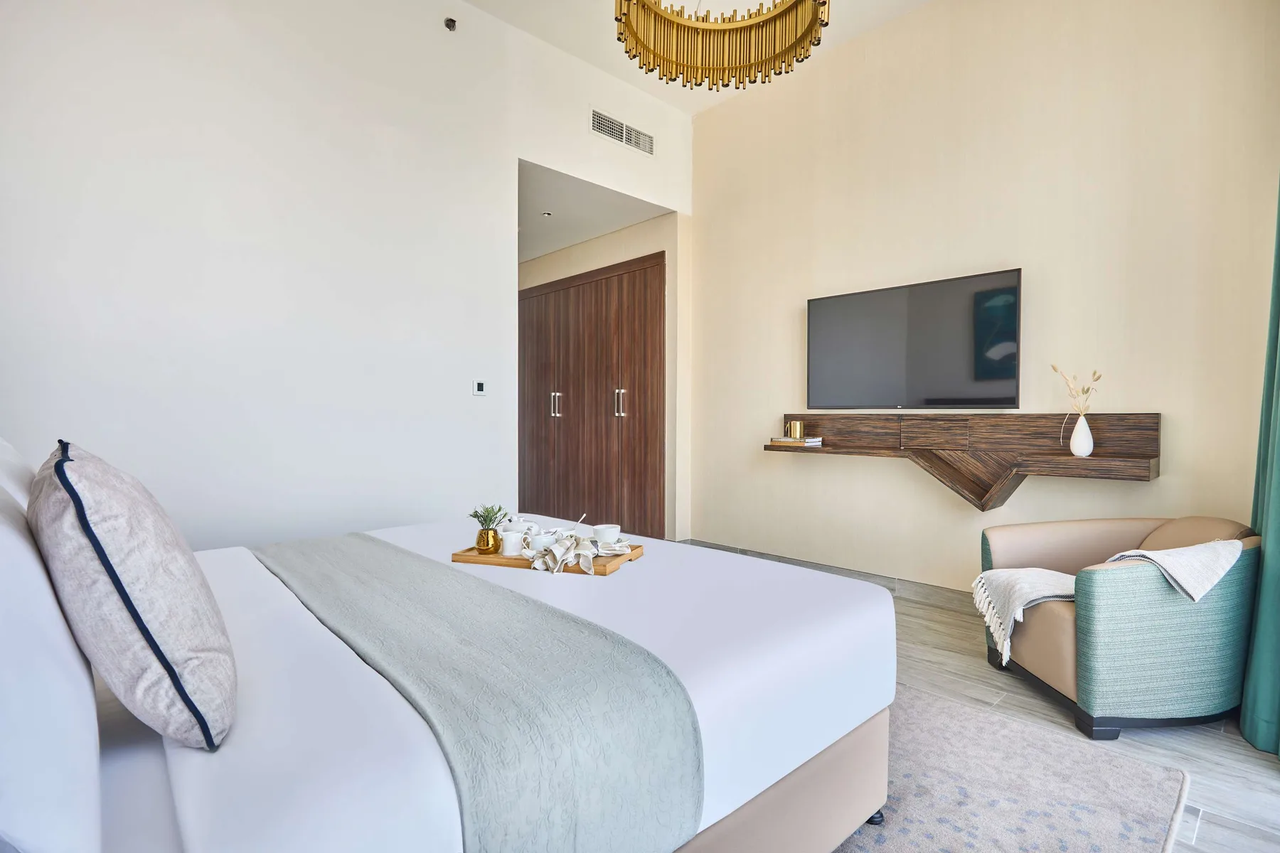 A bedroom with a neatly made bed and a wall-mounted television above a shelf.