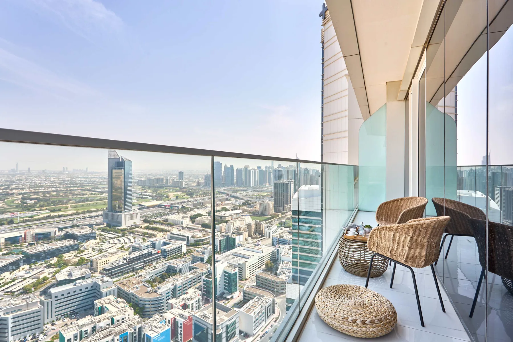 A high-rise balcony with wicker seating overlooks a wide city skyline.