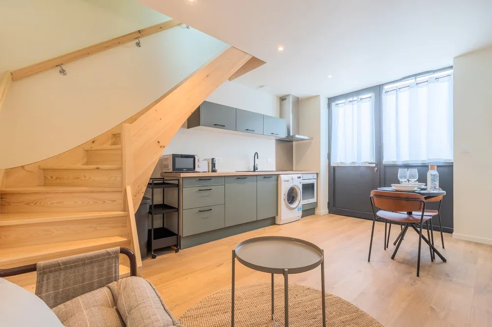 Una luminosa zona de estar tipo estudio con cocina pequeña y escaleras de madera.