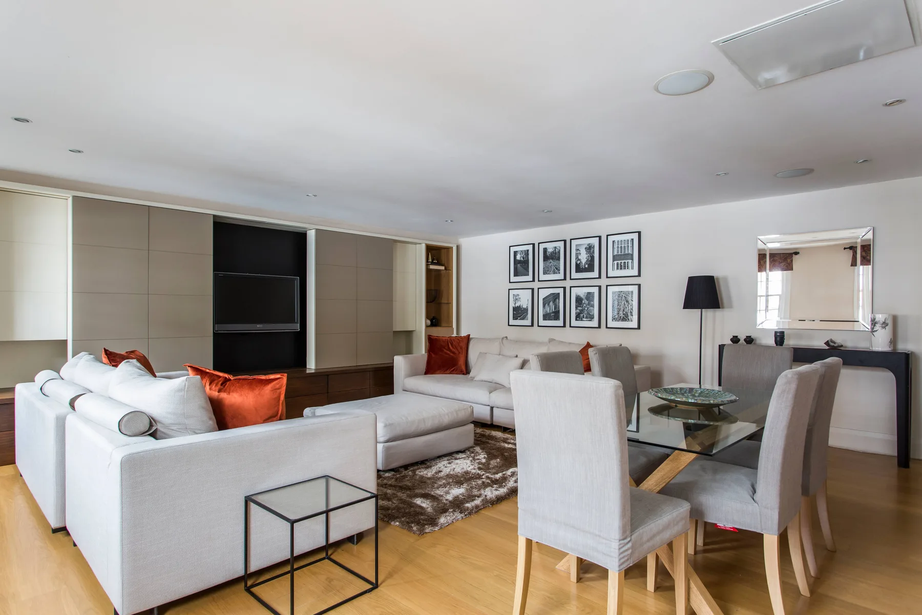 A living and dining area with light seating, a glass table, and framed wall art.