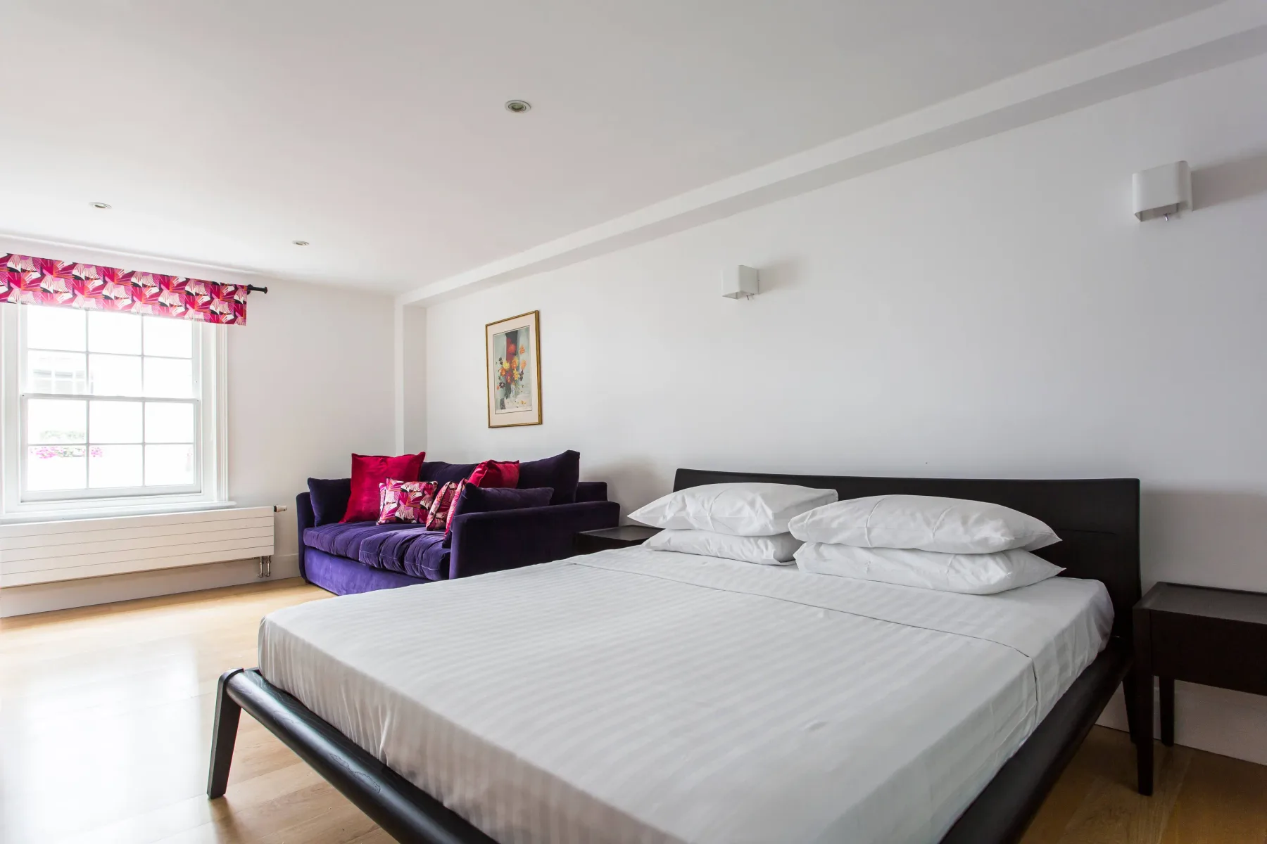 Un dormitorio con una cama grande y una zona de asientos morada junto a la ventana.