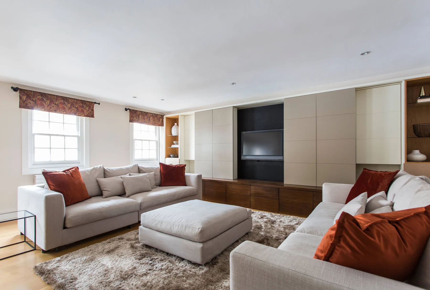 A living room with two seating areas facing a television and a central ottoman.
