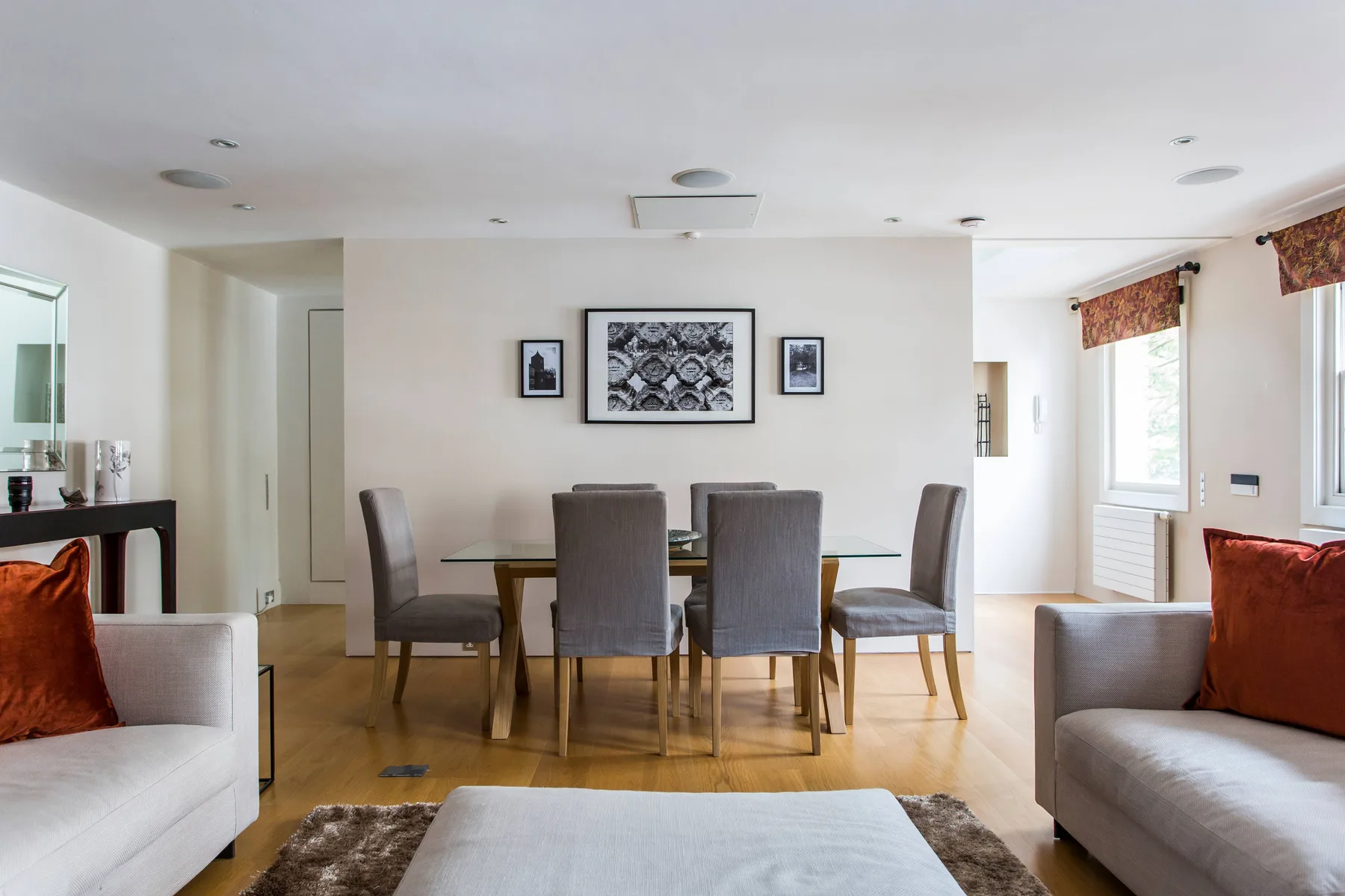 A dining area with a glass table and gray seating sits between two living room sofas.