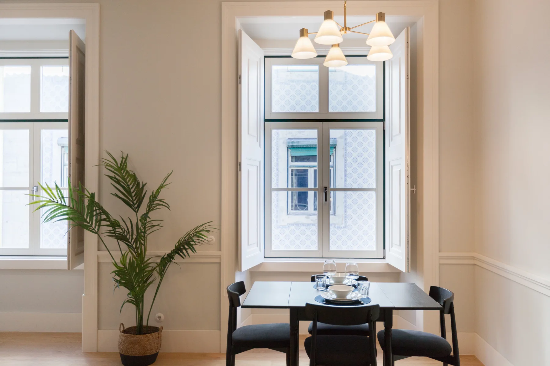 Comedor con una mesa y lámparas colgantes junto a ventanas altas.