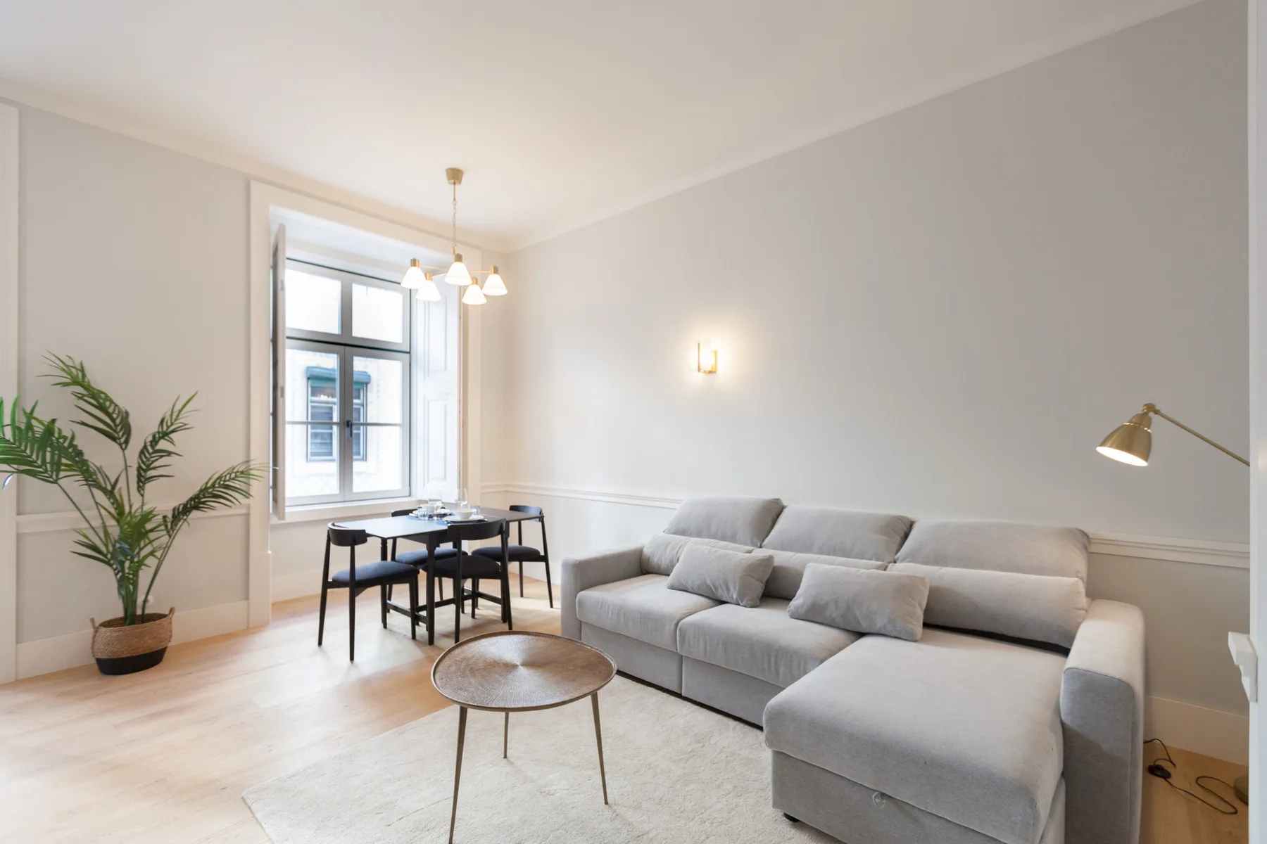 Una sala luminosa con asientos grises, una mesa de centro y un comedor junto a la ventana.