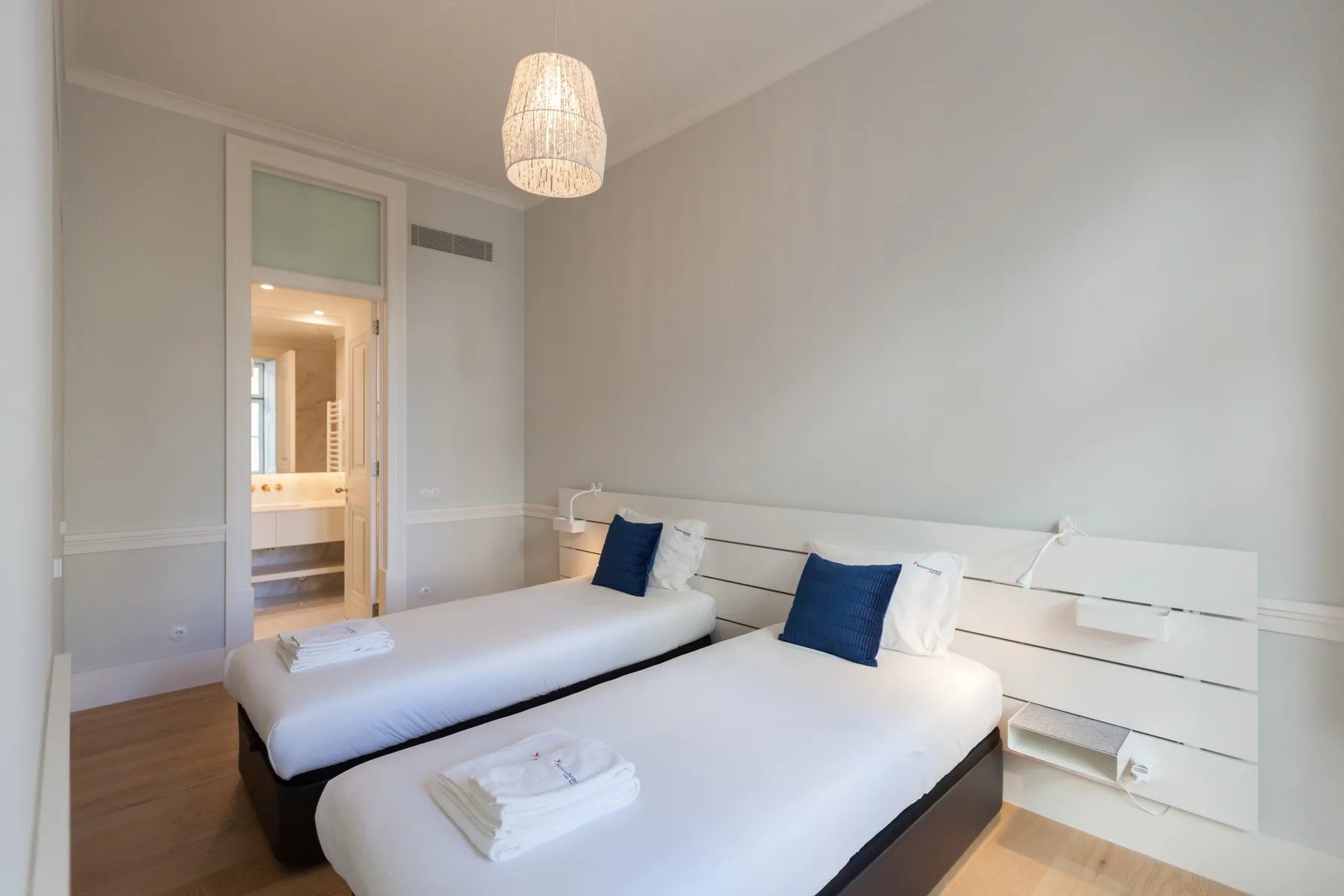 Un dormitorio luminoso con dos camas y un cabecero integrado.