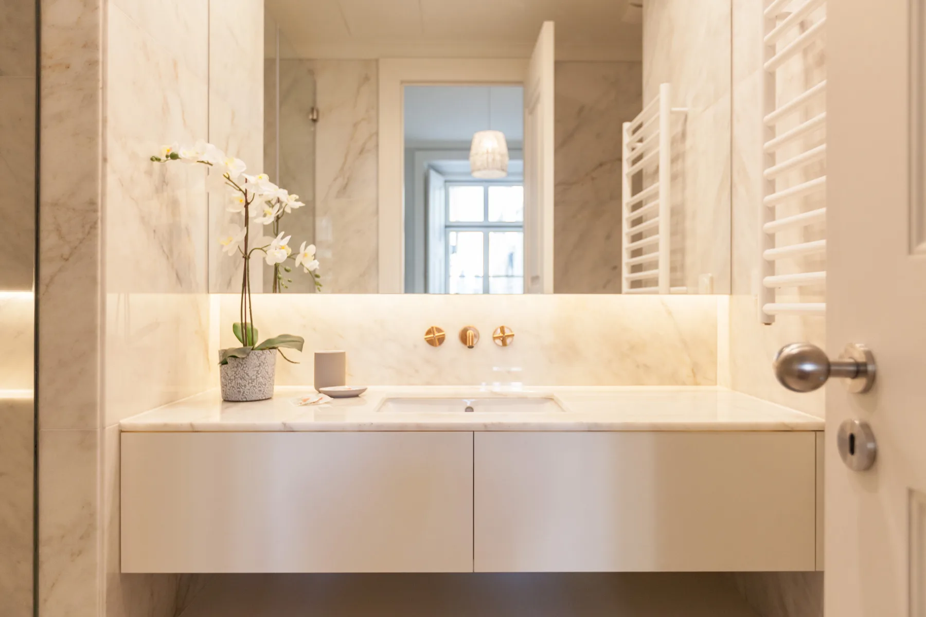 Un lavabo de baño luminoso con un espejo amplio y una pequeña orquídea.
