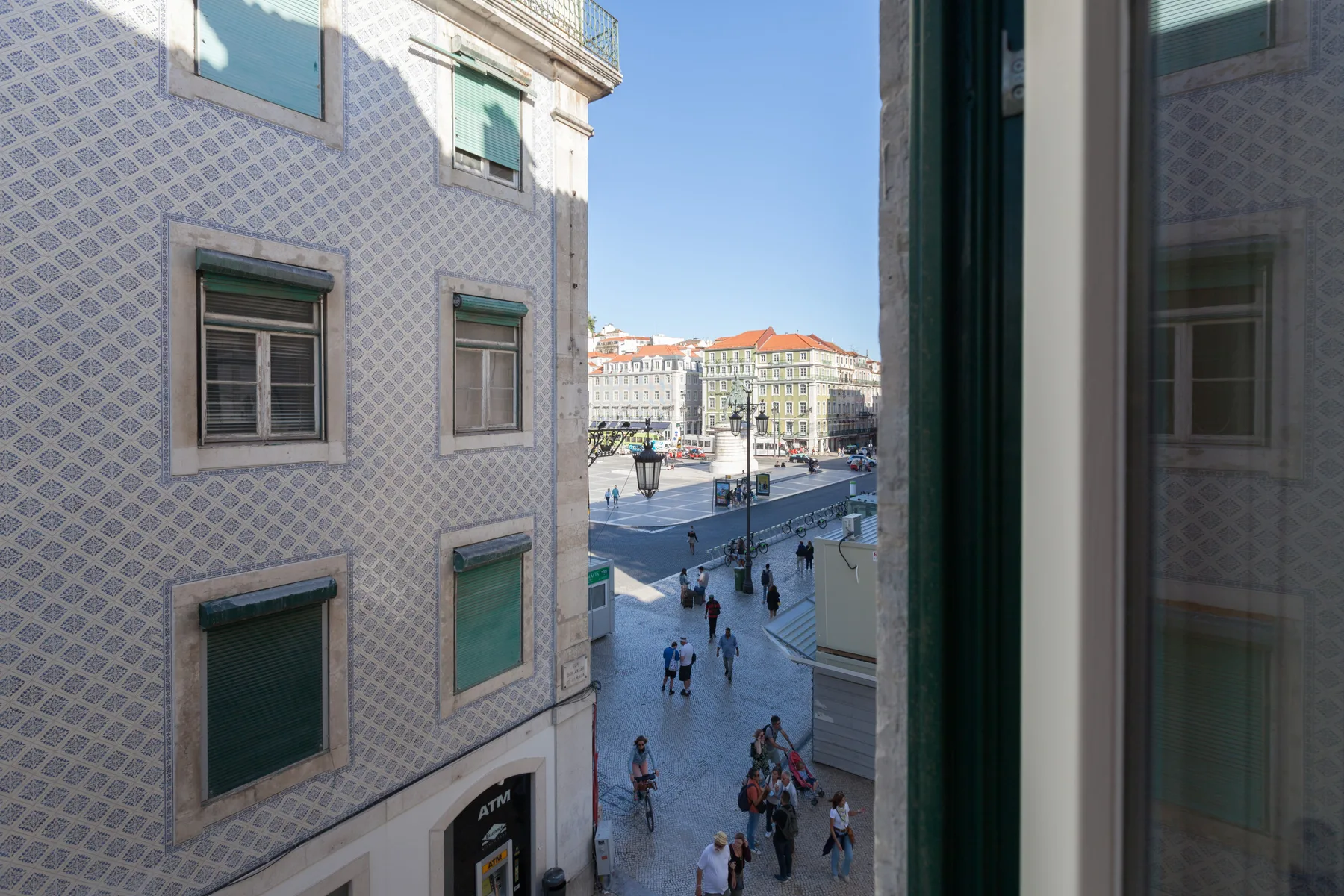 Una vista por la ventana da a una plaza con peatones y edificios alrededor.