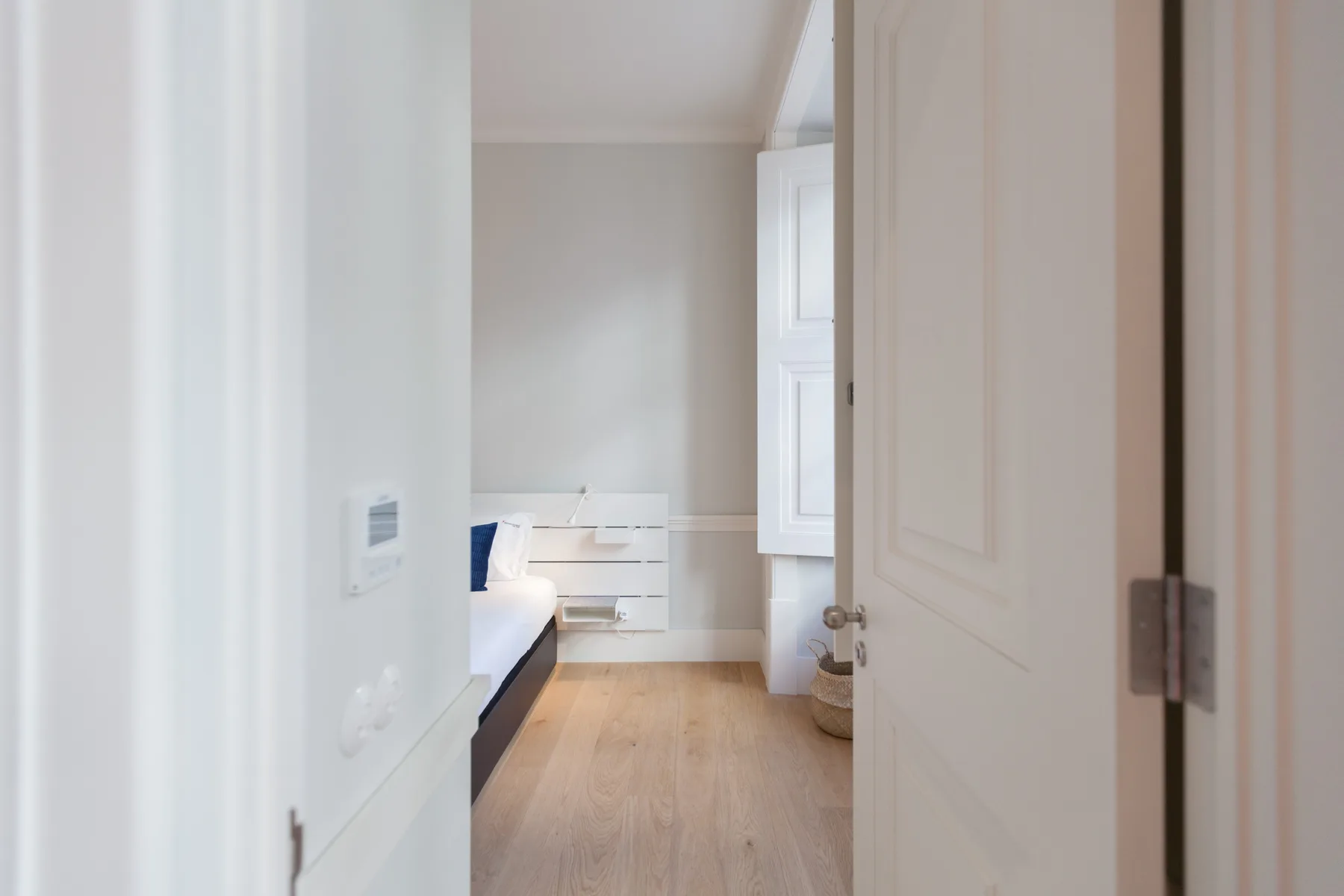 Se ve un dormitorio a través de una puerta abierta, con una cama y suelo de madera clara.