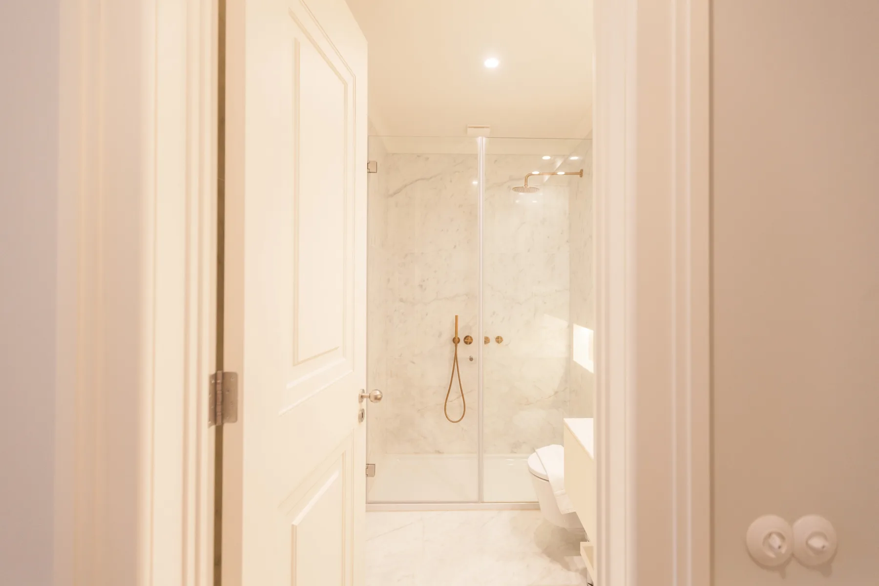 Un baño con una ducha de cristal y paredes claras.
