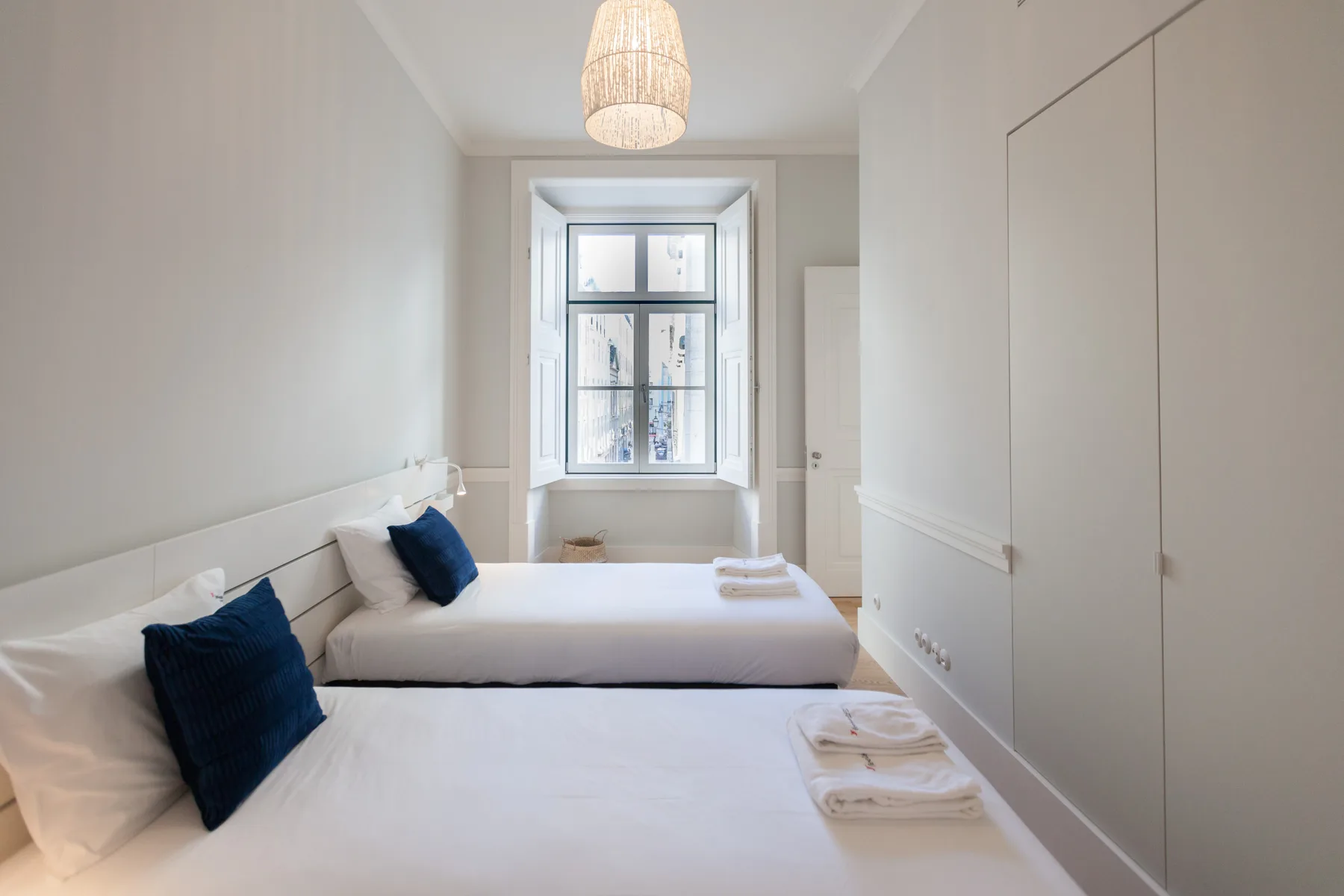 Un dormitorio luminoso con dos camas y una ventana al fondo.