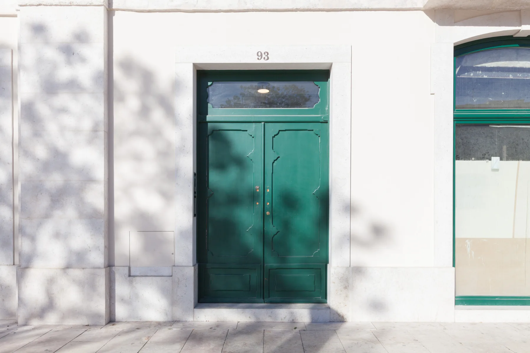Una puerta verde de dos hojas en una pared exterior blanca.