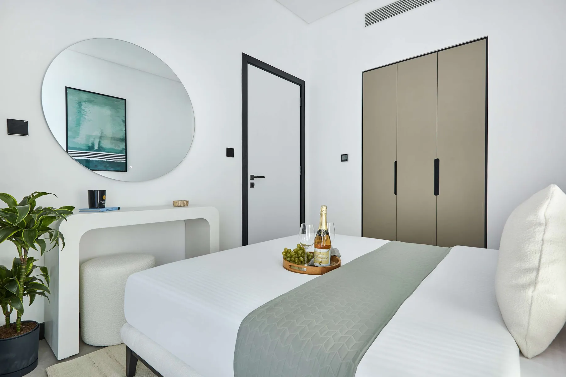 Un dormitorio con una cama bien tendida, un espejo redondo y armarios empotrados.